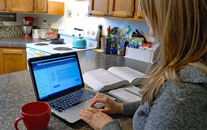An Self-Paced Online EMT Course student completes didactic coursework on her laptop while seated at a dining room counter in her home