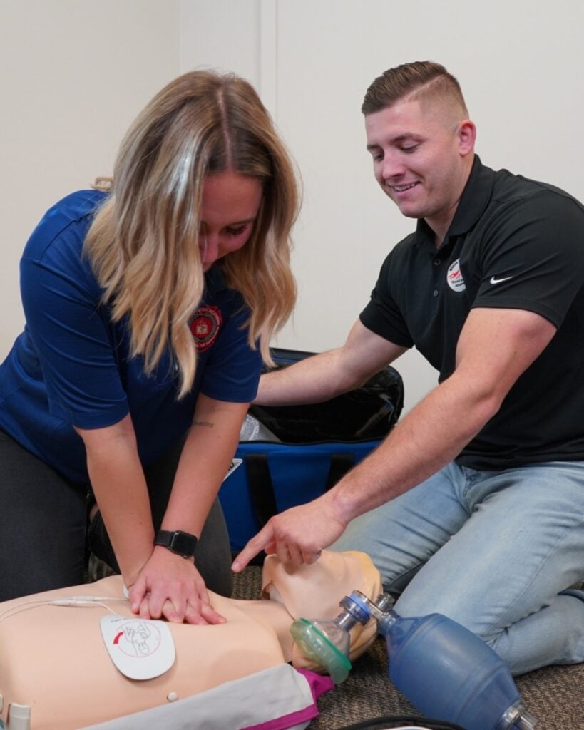 IMA instructor guiding a student through hands-on CPR chest compressions on a training manikin in Boise classroom