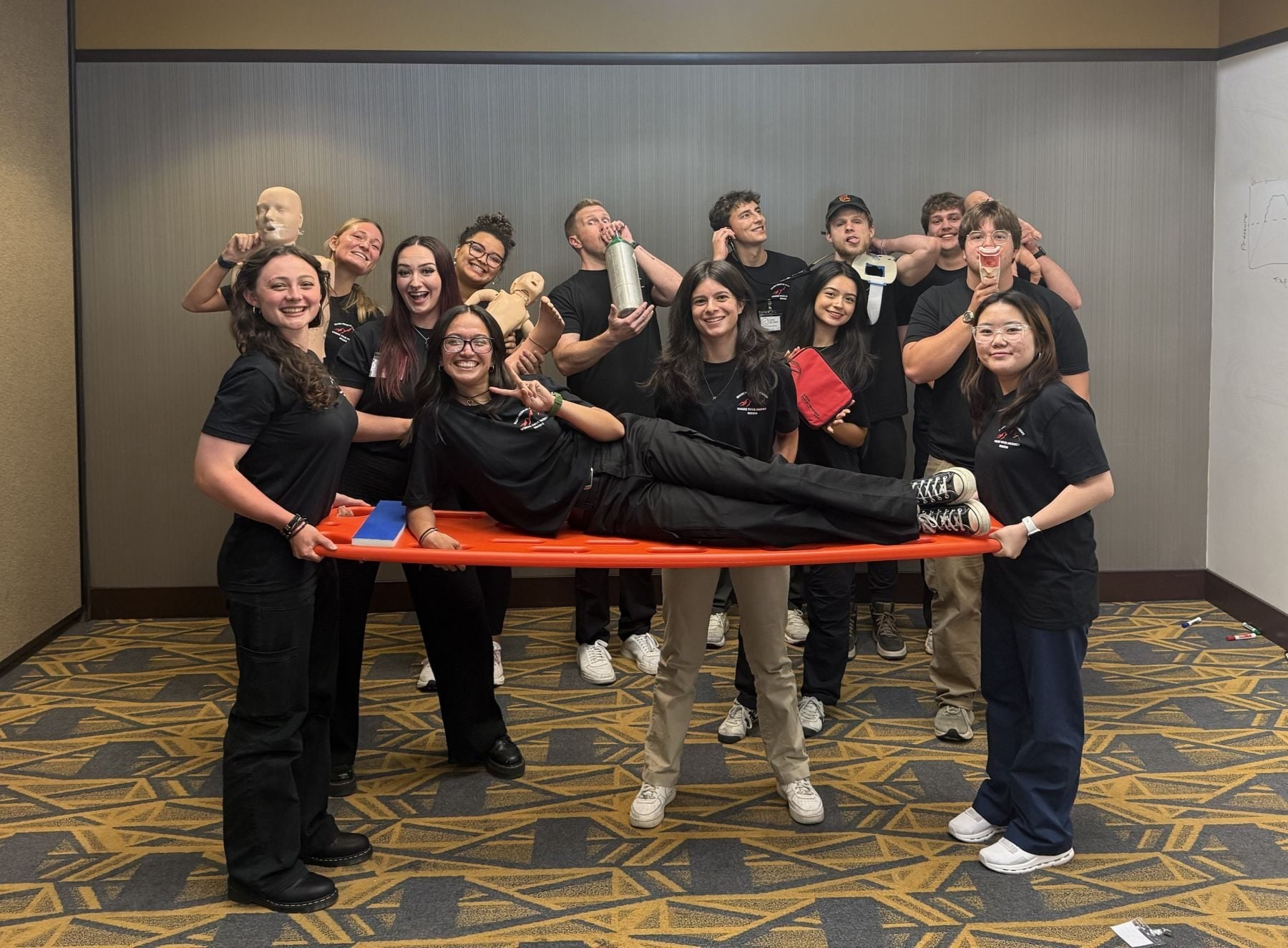EMT students at Idaho Medical Academy's Boise campus during Skills Week, holding a classmate on an orange backboard